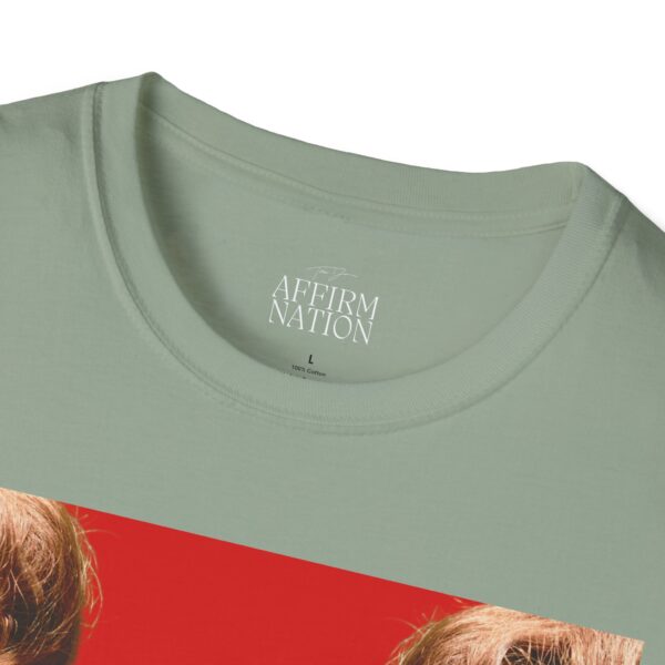Close-up of a pale sage-green crewneck T-shirt showing a white printed label with a handwritten-style signature above the words ‘AFFIRM NATION,’ followed by a large ‘L’ size indicator and ‘100% Cotton’ beneath.